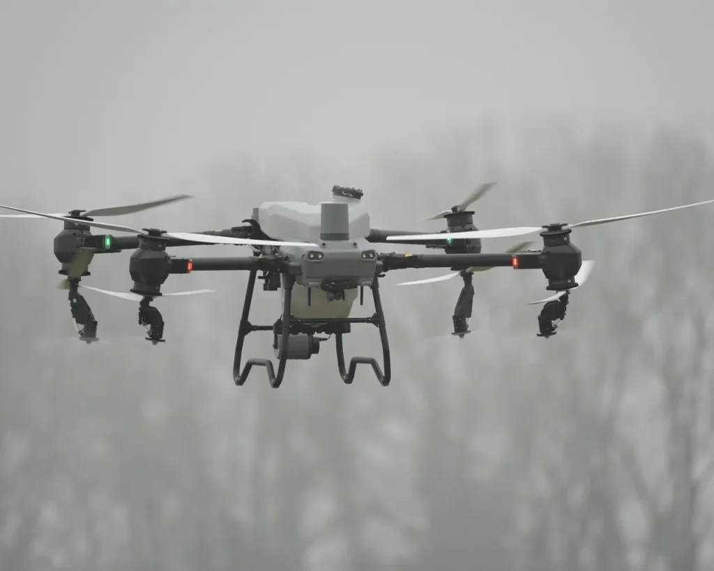 Eine DJI Agras T50 Landwirtschaftsdrohne befindet sich im Flug und sprüht Pflanzenschutzmittel auf ein Feld.