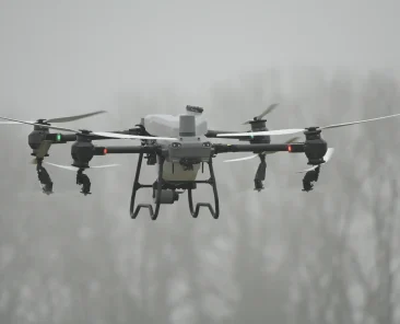 Eine DJI Agras T50 Landwirtschaftsdrohne befindet sich im Flug und sprüht Pflanzenschutzmittel auf ein Feld.