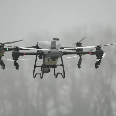 Eine DJI Agras T50 Landwirtschaftsdrohne befindet sich im Flug und sprüht Pflanzenschutzmittel auf ein Feld.